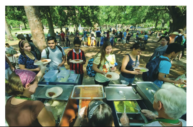 Students receiving Krishna Lunch from a serving line beneath trees